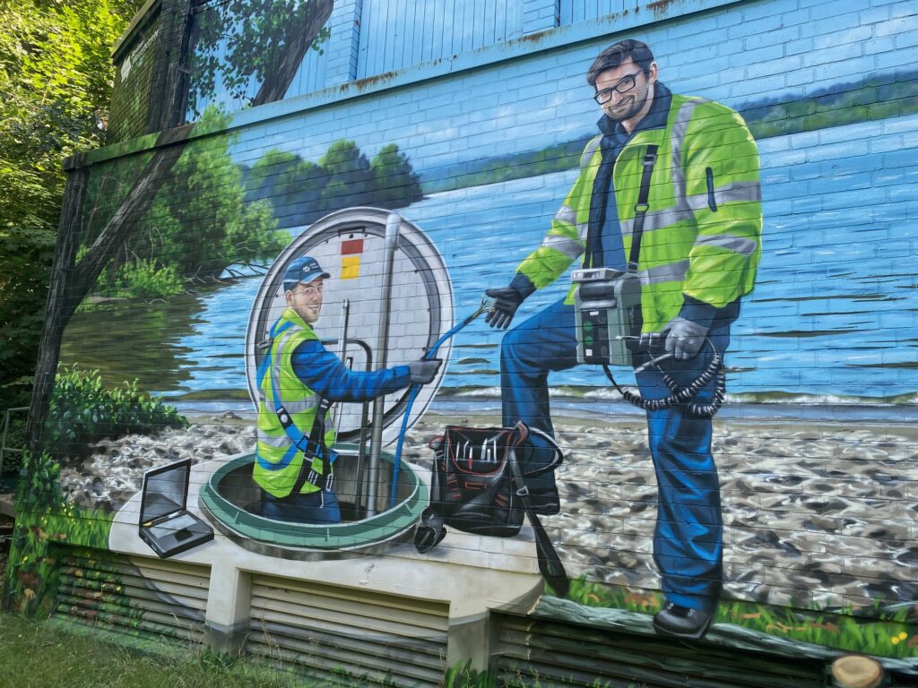 Wandgemälde am Wasserwerk, das zwei Arbeiter zeigt, von denen einer in einen Grundwasserbrunnen hinabsteigt.
