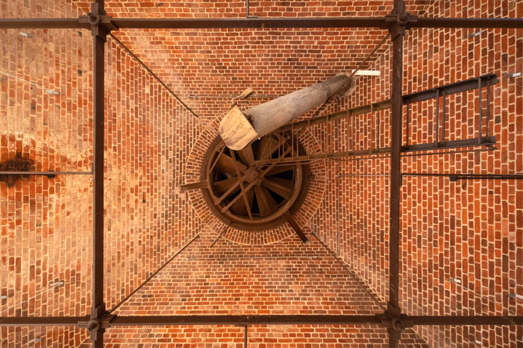 Blick nach oben auf eine Backsteindecke mit Metallelementen und einer runden Öffnung in der Mitte.