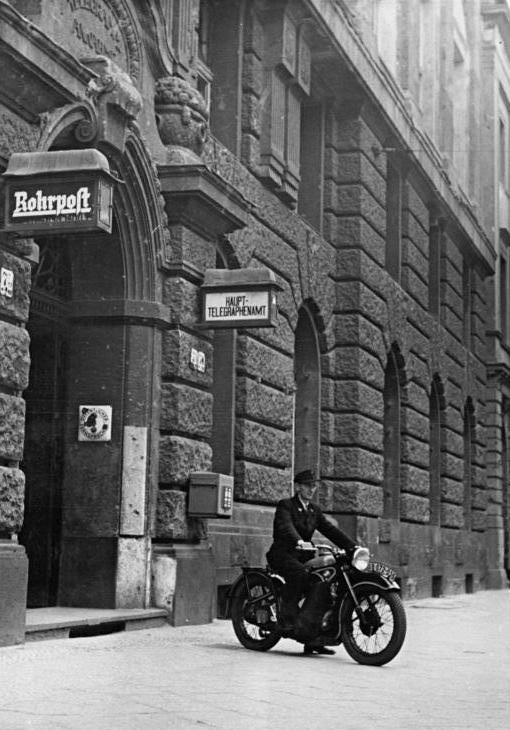Postbote auf BMW-Motorrad vor Haupttelegrafenamt, Schild "Rohrpost" neben Eingang