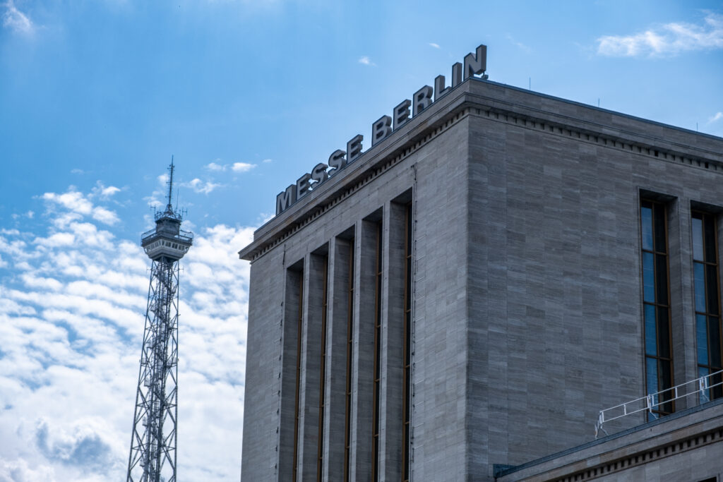 Außenansicht der Messe Berlin bei blauem Himmel mit dem Funkturm im Hintergrund.
