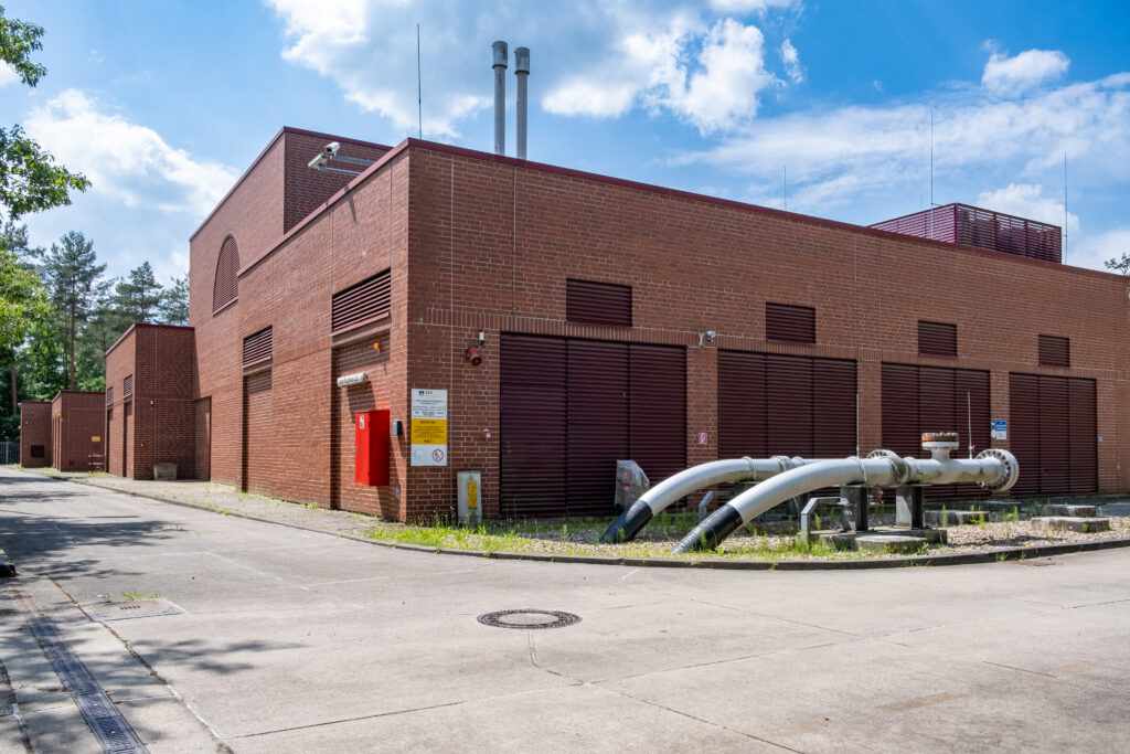 Außenansicht des zum Erdgasspeicher gehörenden Gebäudes mit Rohren, die davor aus der Erde kommen.