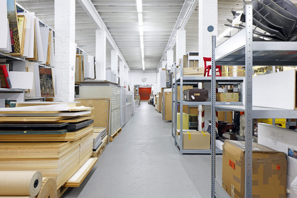 Im Depot stehen Regale mit verpackten Objekten und aufgereihten Gemälde, sicher verpackt und geschützt vor Schäden.