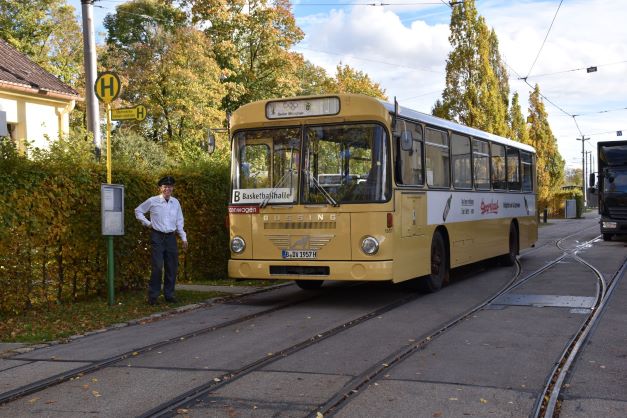 Ein historischer Bus steht an einer Haltestelle. Der Busfahrer steht draußen und schaut in die Kamera.