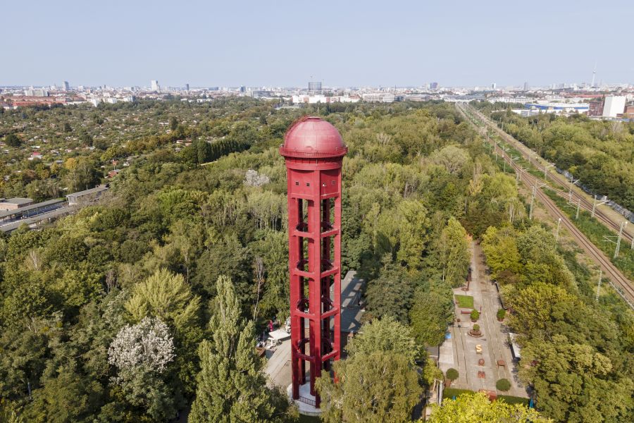 Foto aus der Vogelperspaktive über den Park. Zwischen den Bäumen ragt ein roter Wasserturm empor.