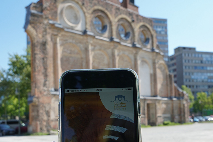 Ein Smartphone wird vor die Überreste des ehemaligen Anhalter Bahnhofs gehalten. Die Webanwendung auf dem Bildschirm zeigt das einst prächtige Gebäude.