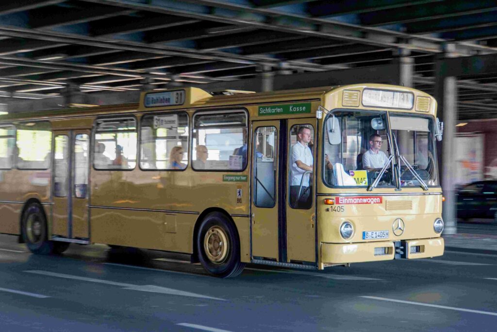 Ein gelber Oldtimerbus fährt eine Straße entlang.