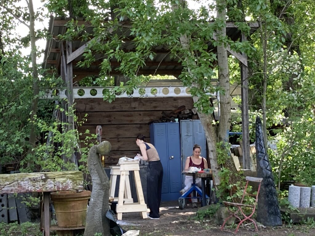 Künsterlinnen arbeiten an ihren Skulpturen im Freien.
