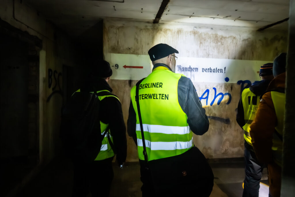 Führung mit Taschenlampen im Bunker. Ein Mann trägt eine gelbe Warnweste.