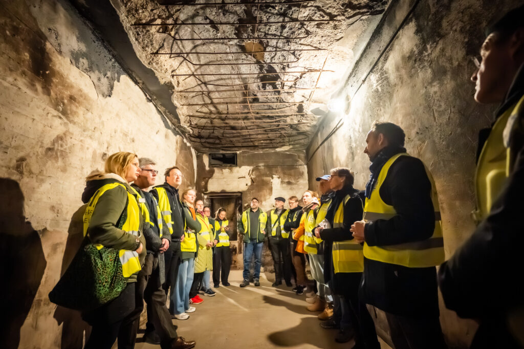 Gruppe während einer Führung in einem Bunker. Alle tragen gelbe Warnwesten.