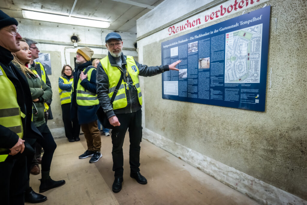 Menschen stehen mit gelben Warnwesten in der Ausstellung in einem Bunker.