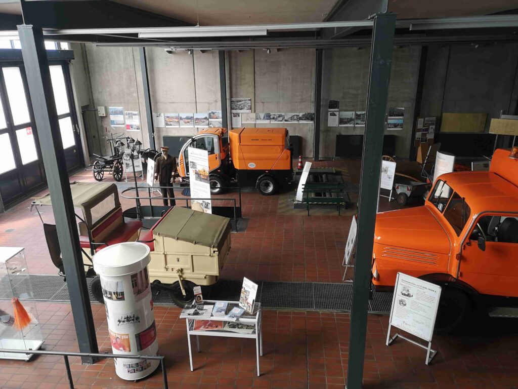 Historische Straßenreinigungsmaschinen stehen in einer Ausstellung.