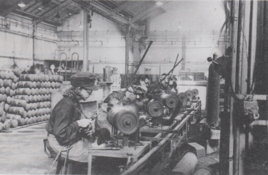Historisches Foto von der Munitionsherstellung in Reinickendorf. Eine Frau arbeitet an einer Maschine.