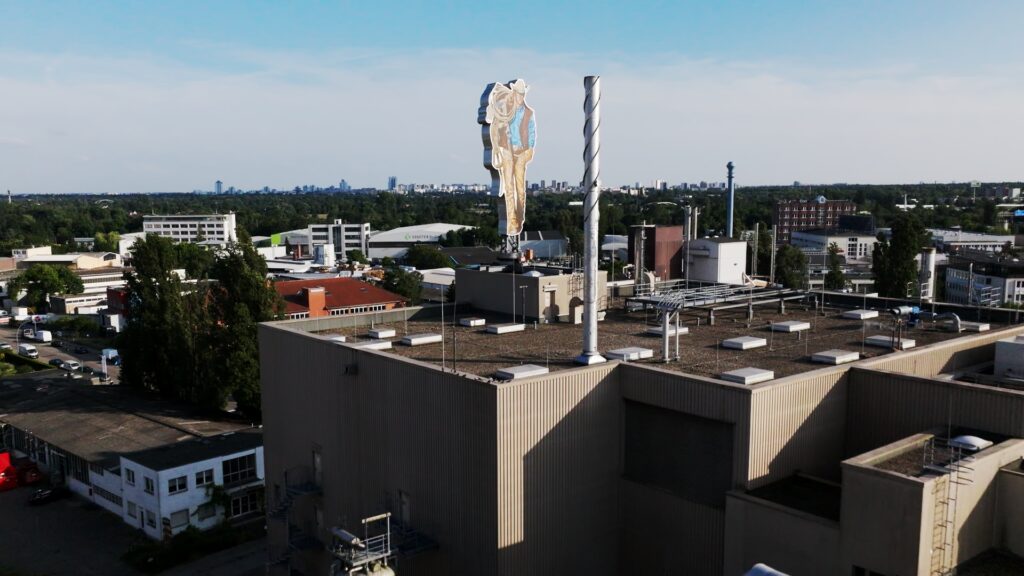 Vogelperspektive auf das ehemalige Werksgelände von Philip Morris. Auf dem Dach ist die Statue einer Werbefigur montiert.