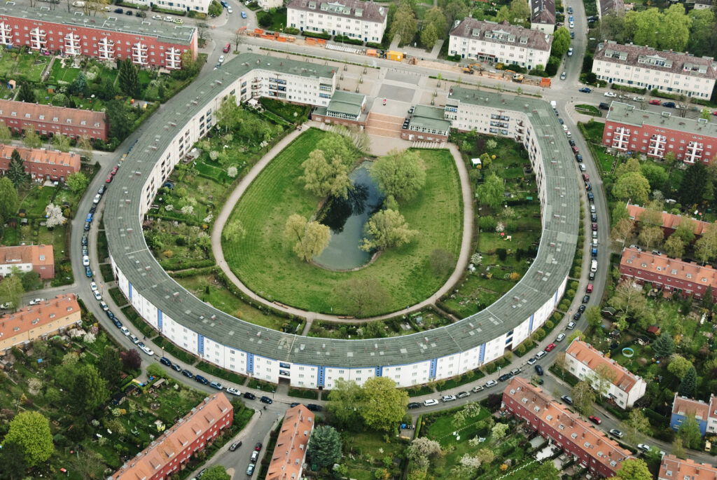 Luftbilder einer Wohnsiedlung. Ein Gebäude ist in Form eines Hufeisens um eine Grünfläche angelegt.