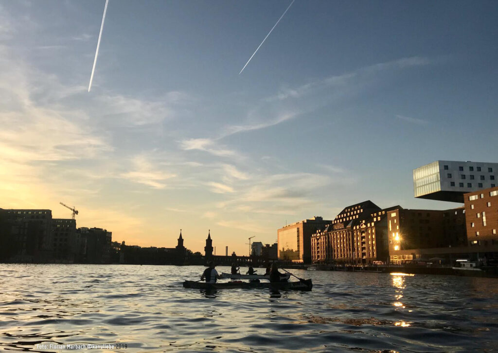 Drei Kanufahrer paddeln im Sonneruntergang auf der Spree.