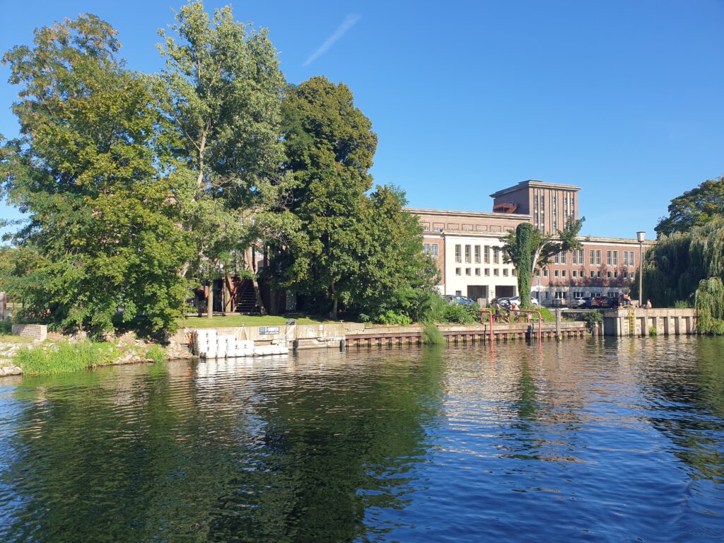 Dunkelbraunes Gebäude mit kleinem Turm vom Fluss aus
