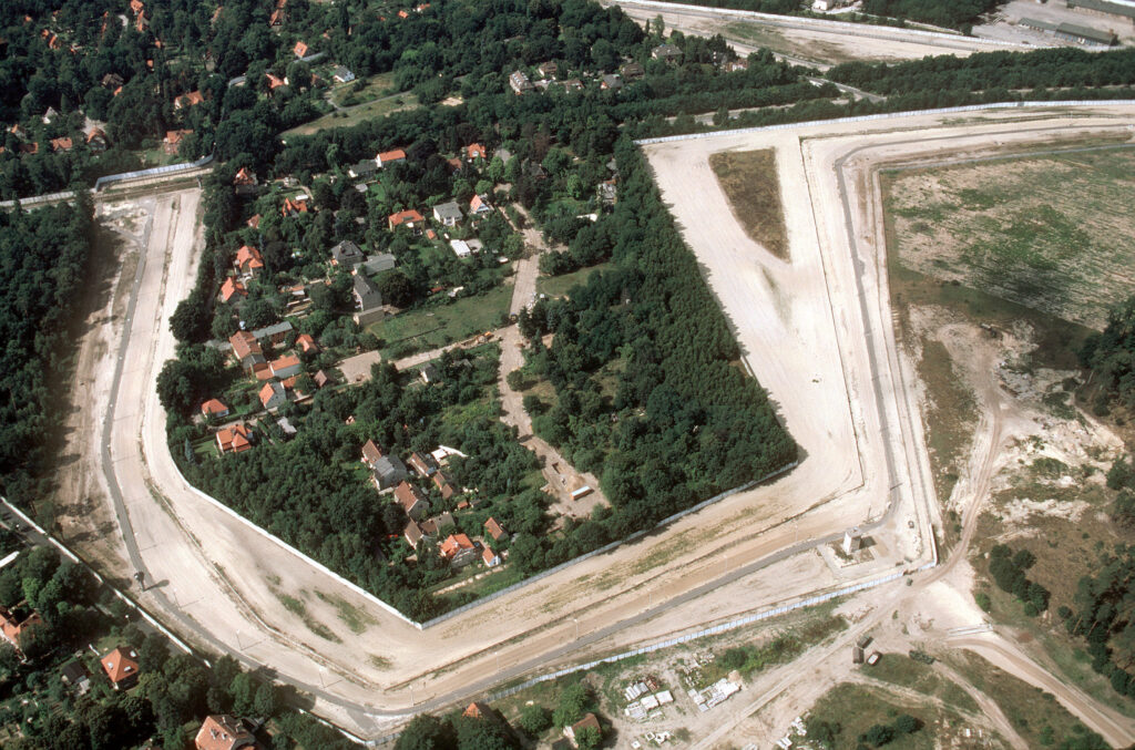 Luftbild der Berliner Mauer 1989 mit einem Knick, in dem Häuser und Grünflächen sind