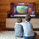 Zwei Jungs im Alter zwischen 4 und 10 Jahren sitzen vor einem alten Röhrenbildschirm und schauen Fernsehen.