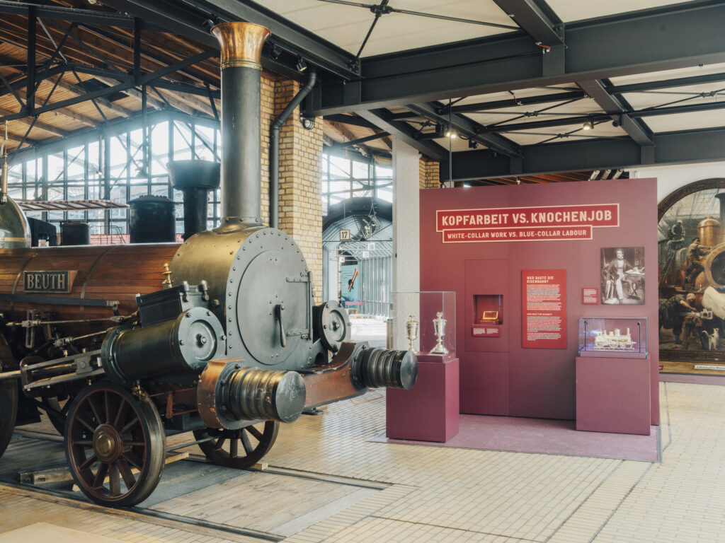 Blick in die Ausstellung Schienenverkehr mit historischer Dampflok und roter Ausstellungswand