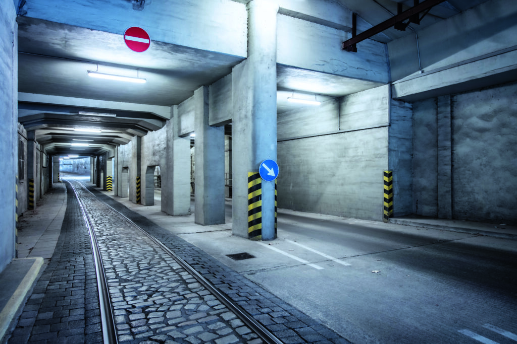 Ein Foto der unterirdischen Tunnelanlagen mit künstlichem Licht. Linkerhand sieht man Bahngleise. Im Hintergrund ist klein der Tunnelausgang zu erkennen.