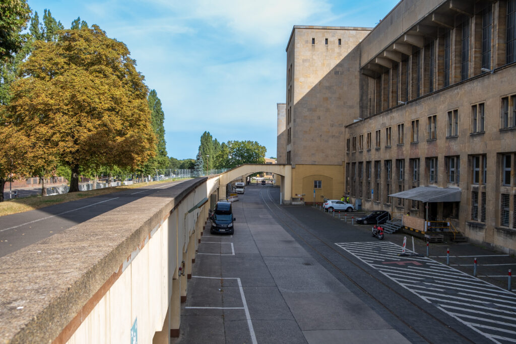 Aufnahme des überirdischen Teils der Gleise, die vor dem Flughafengebäude entlanglaufen. Links neben den Gleisen verläuft eine Mauer, daneben die Straße.