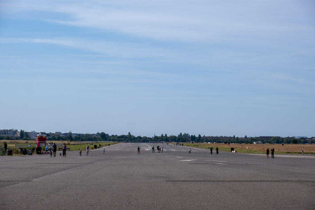 Ein Ausblick über die weitläufige Start- und Landebahn. Man sieht einige Menschen auf der Bahn, die aufgrund der Entfernung sehr klein wirken. Der meiste Teil des Fotos besteht aus blauem Himmel über der Bahn.
