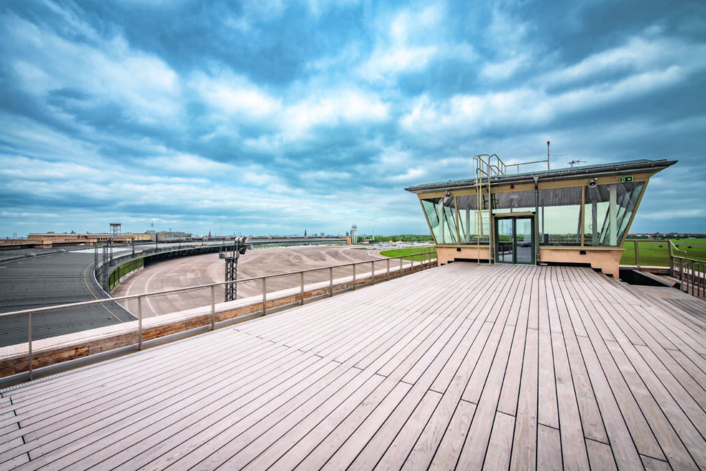 Dynamisch fotografierter Ausblick von der Dachterrasse des THF Towers. Das Foto ist perspektivisch verzerrt. Im Hintergrund sind markante graue Wolken über dem restlichen Gelände zu sehen.