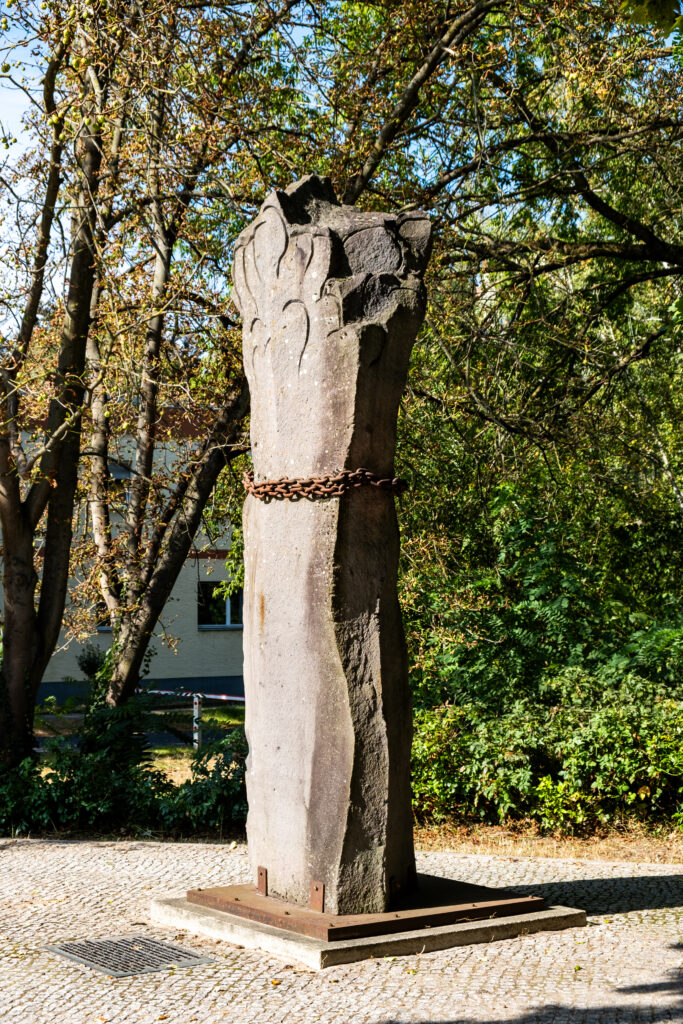 Die aus grauem Stein gefertigte Säule der Gefangenen steht vor einigen Bäumen.