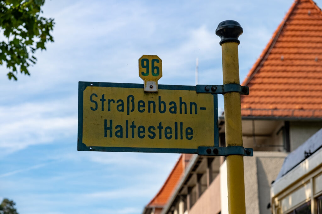 Aufnahme eines Schilds vor blauem Himmel. Auf gelbem Grund steht in schwarz die Nummer 96 und "Straßenbahn-Haltestelle".