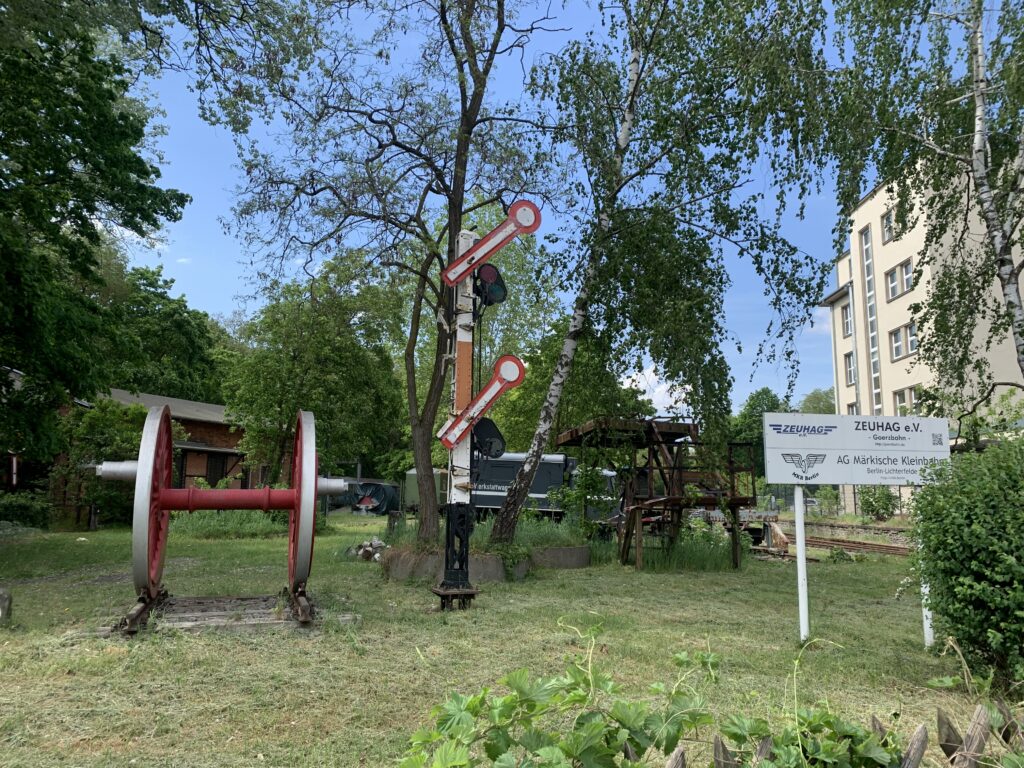 Zwischen Birken stehen auf einer Wiese diverse Gerätschaften wie eine Signalanlage, die von der Goerzbahn stammen.
