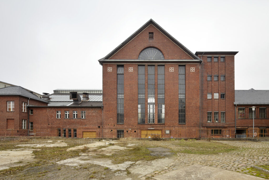 Außenansicht des aus Backstein errichteten Maschinenhauses des Kraftwerks Steglitz vor bewölktem Himmel.