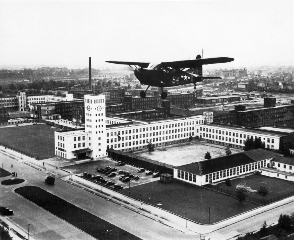Historische, schwarz-weiße Luftaufnahme von einem Flugzeug vor dem Telefunke-Werk in Zehlendorf.