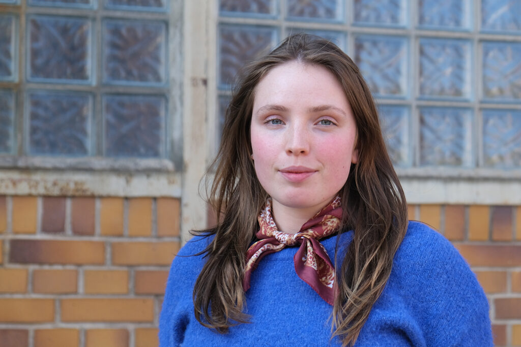 Teamfoto von Malisa Quander. Sie steht vor einer Backsteinwand und blickt in die Kamera.
